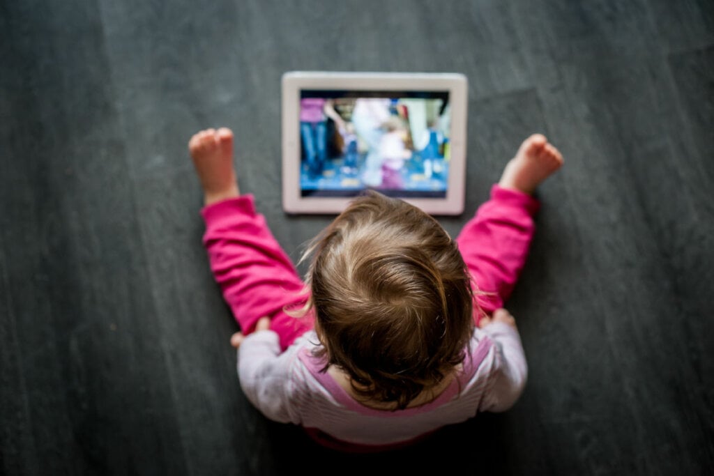 criança sentada no chão olhando para a tela do tablet