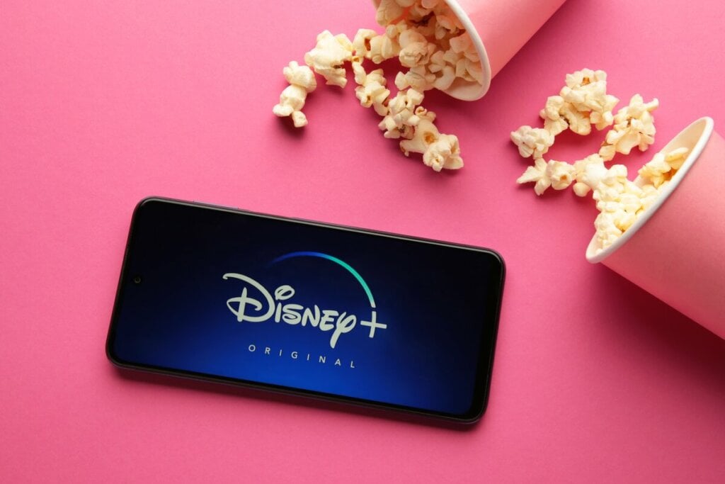 Logo do Disney Plus e um celular com copos de pipoca rosa ao lado