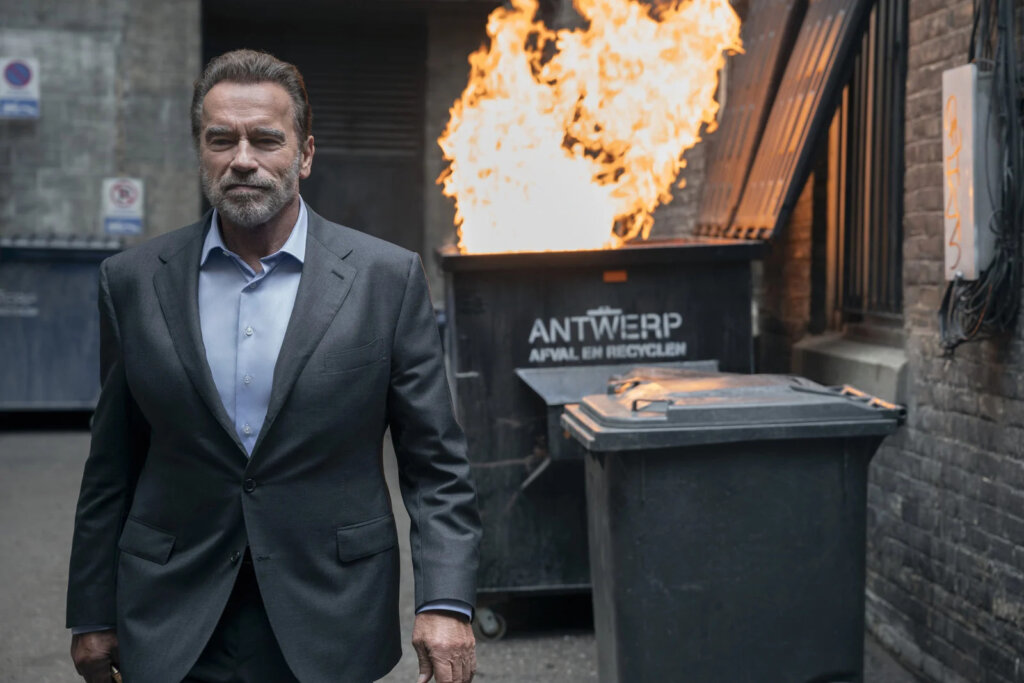 Imagem de Arnold Schwarzenegger com uma lata de lixo pegando fogo no fundo