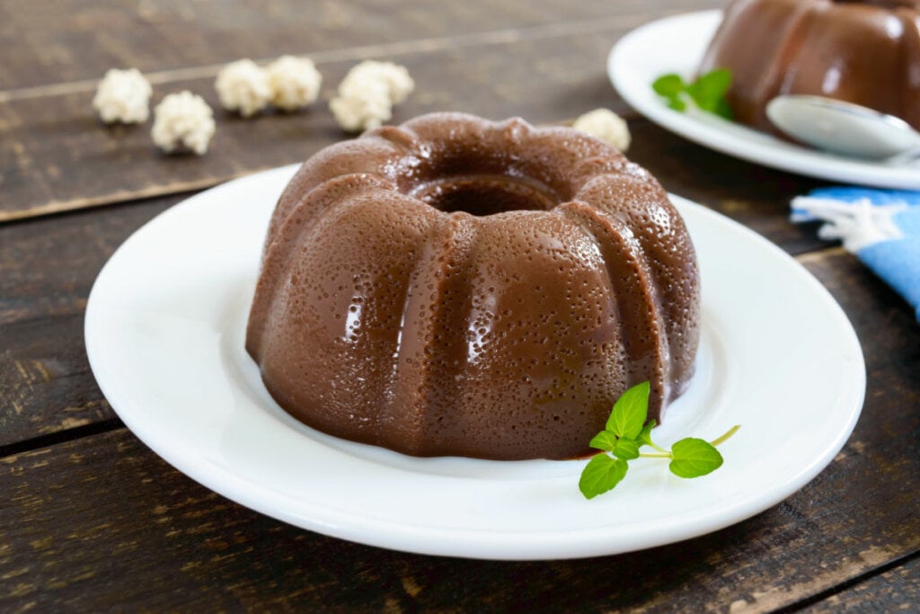 Pudim de chocolate em pratos brancos; fundo escuro de madeira