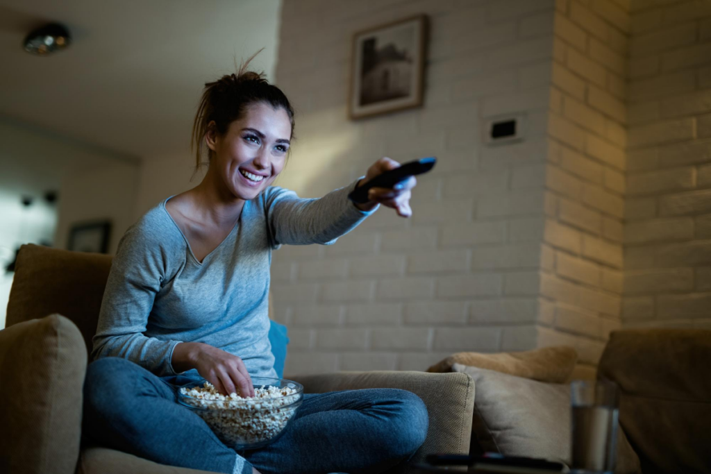 Mulher apontando controle para televisão enquanto come pipoca