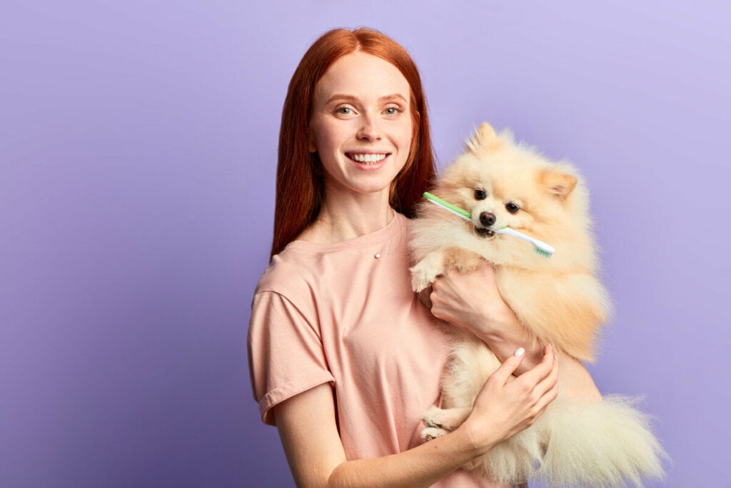 Mulher com cabelo ruivo segurando cachorro com escova de dente na boca