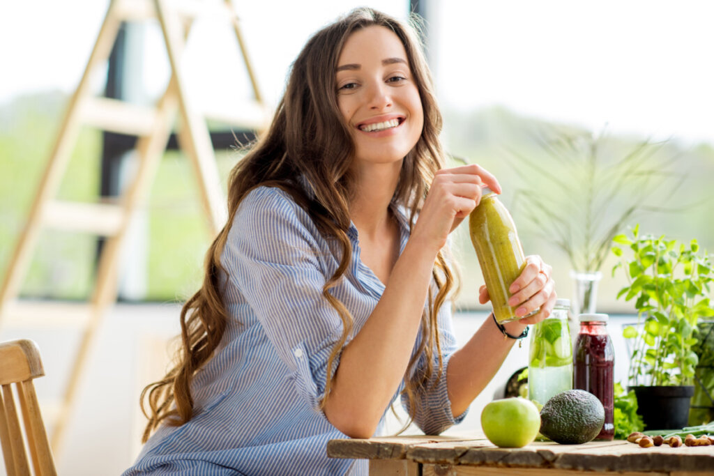 Mulher feliz sentada com bebidas e comida verde saudável em casa. 
