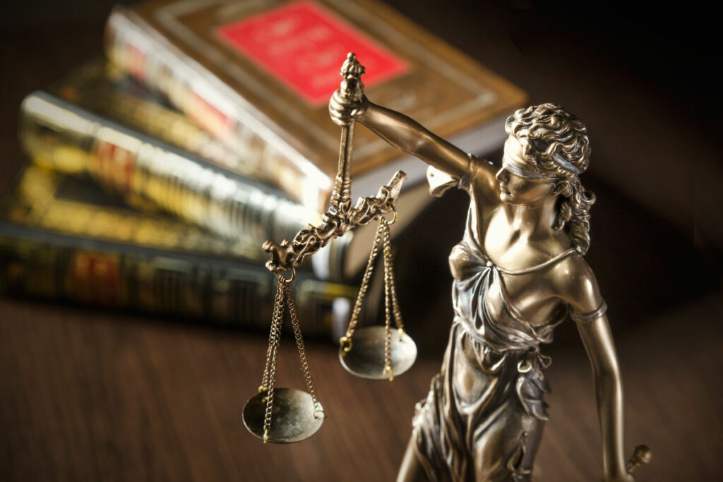 Pequena escultura do símbolo da Justiça com livros de Direito atrás