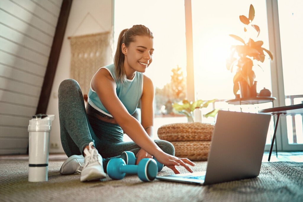 Mulher com roupa de academia sentada mexendo em um notebook