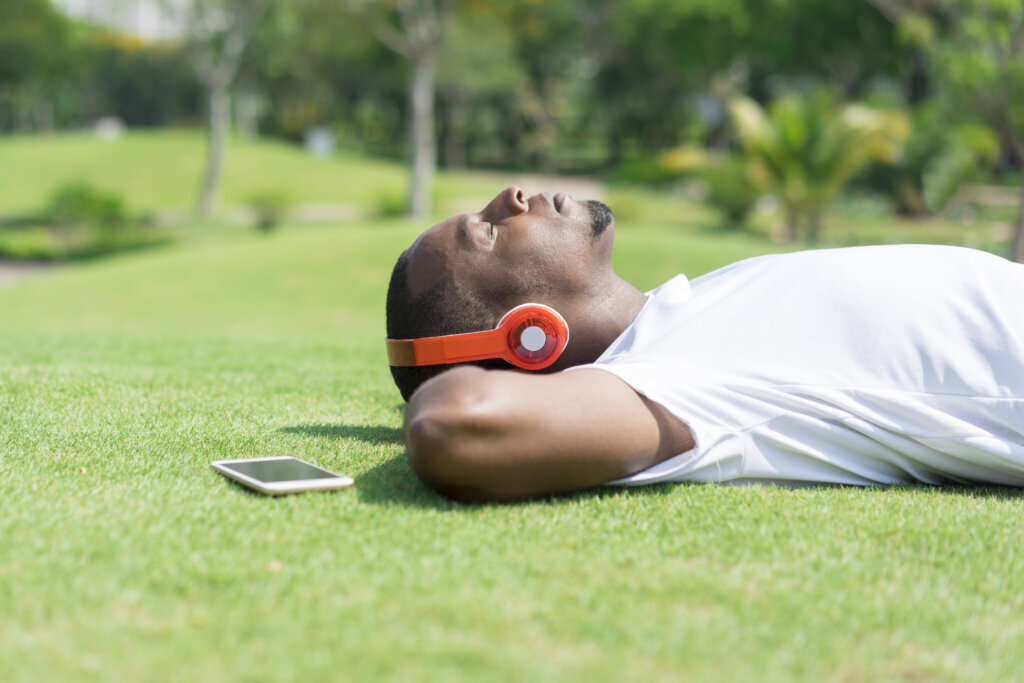 Homem calmo deitado em gramado de olhos fechados e ouvindo música