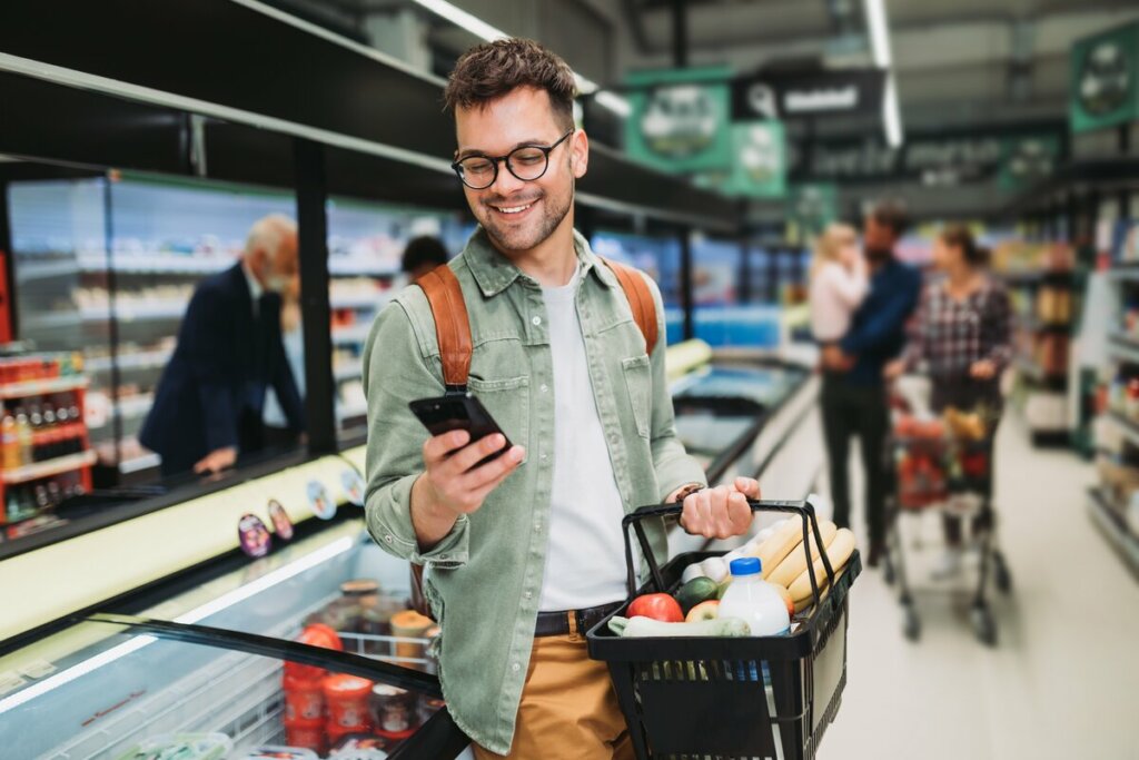Homem sorrindo mexendo no celular em um supermercado