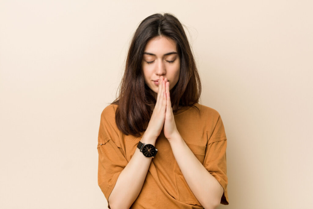 Mulher com camiseta marrom, olhos fechados e rezando
