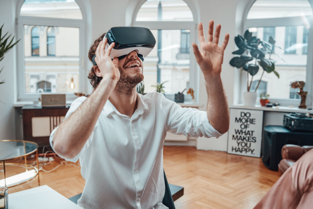 Homem sentado em sala com óculos de realidade virtual interagindo com imagens.