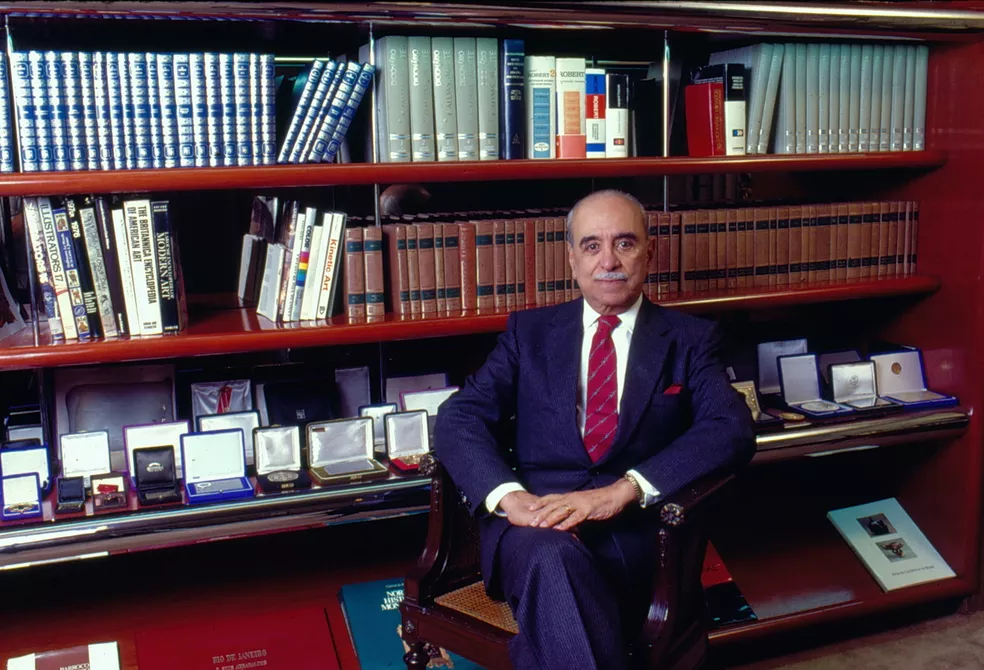 Roberto Marinho sentado em escritório rodeado de livros e prêmios