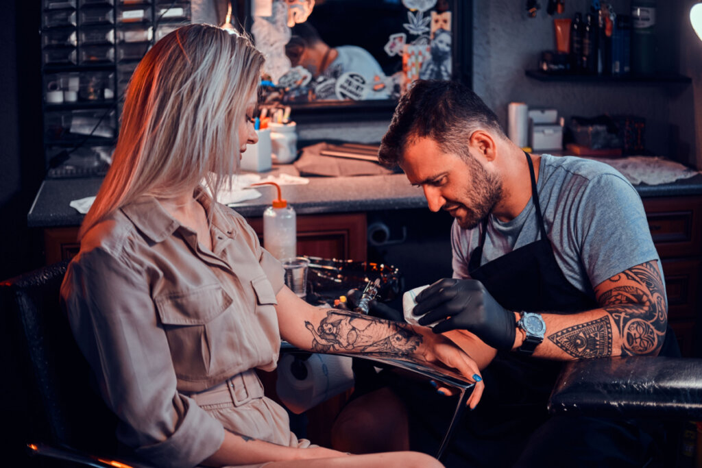 Tatuador focado criando uma nova tatuagem na mão de uma jovem no estúdio.