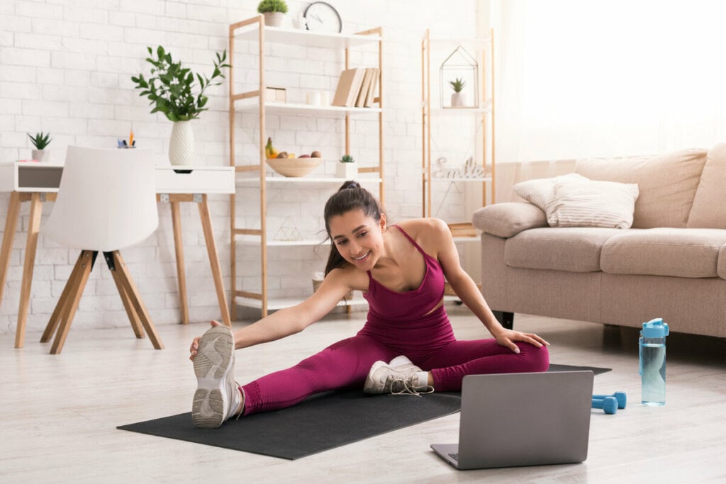 Mulher fazendo pilates em uma sala de estar com notebook