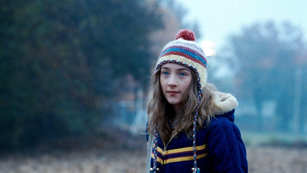 Imagem do filme "Um olhar do paraíso". Menina de gorro e blusa de frio em cenário de campo.
