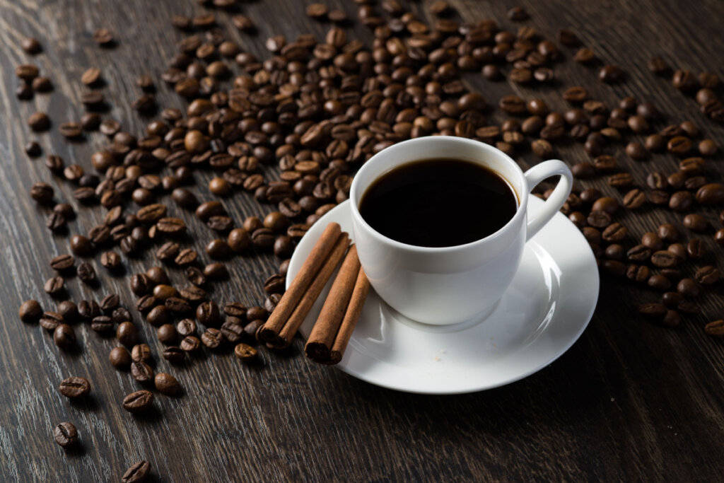 Uma xícara de café branca sob mesa de madeira com vários grãos de café espalhados por cima
