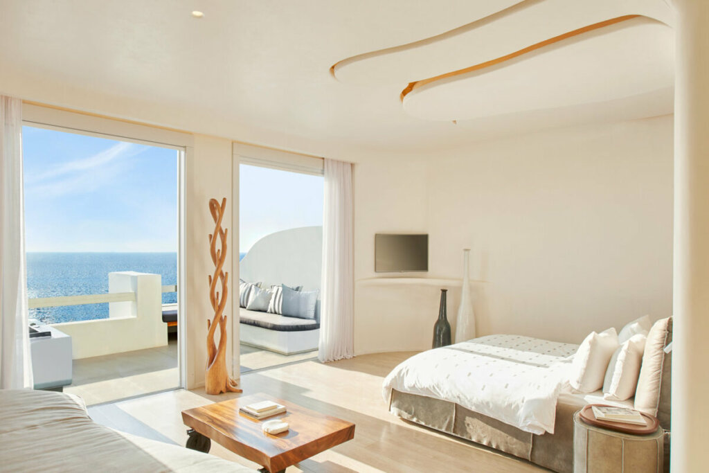 Quarto com cama branca e vista para o mar no hotel Cavoo Tagoo Mykonos 