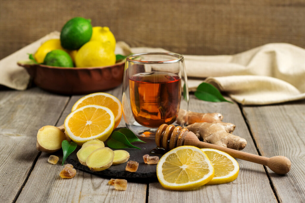 Xícara de vidro com chá, com mel e rodelas de limão, gengibre e laranja, em cima de uma mesa de madeira 