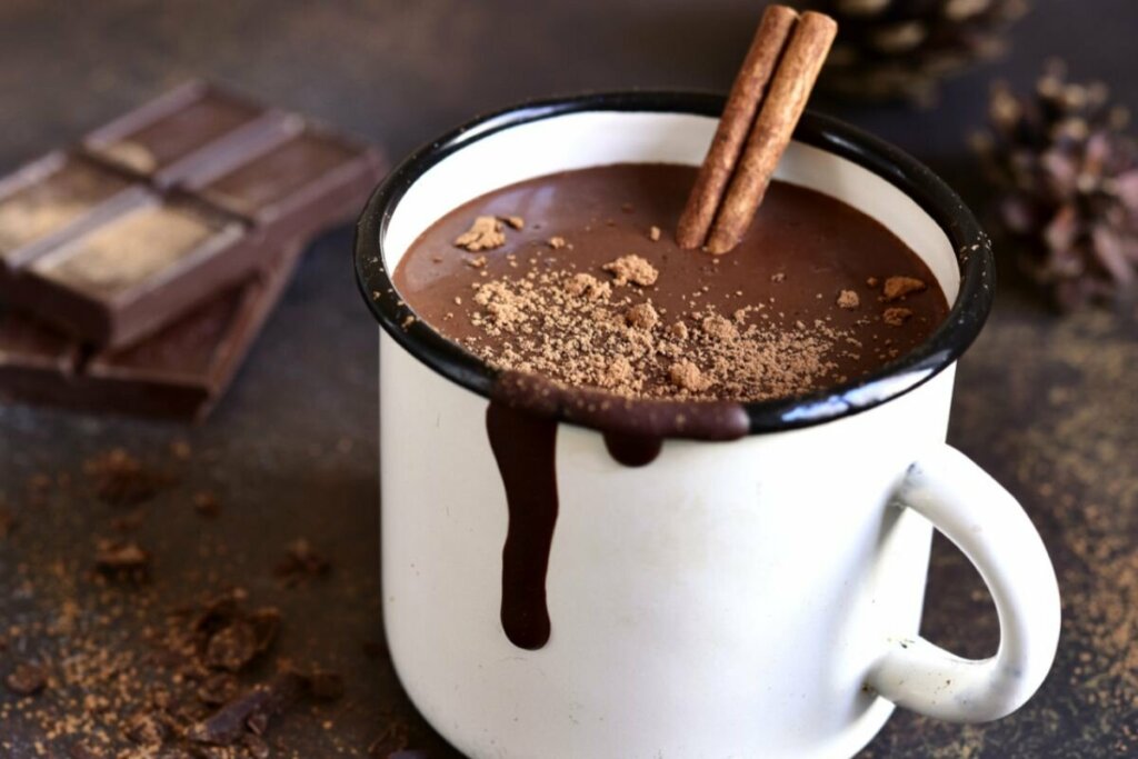 Chocolate quente vegano em uma xícara branca e decorado com dois paus de canela