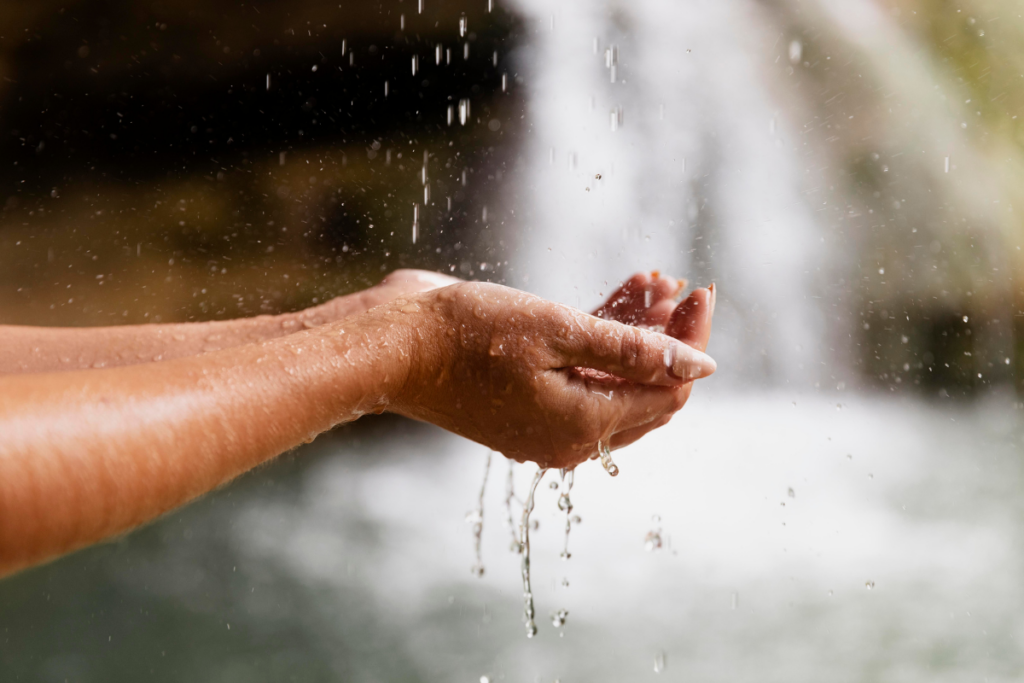 Mãos em forma de concha com água da chuva caindo em cima das mãos