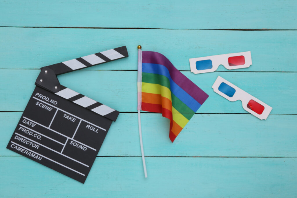 Bandeira do arco-íris LGBT com óculos 3D, claquete de filme sobre fundo azul de madeira.