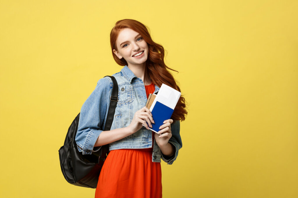 Mulher sorrindo com mochila nas costas e segurando um passaporte