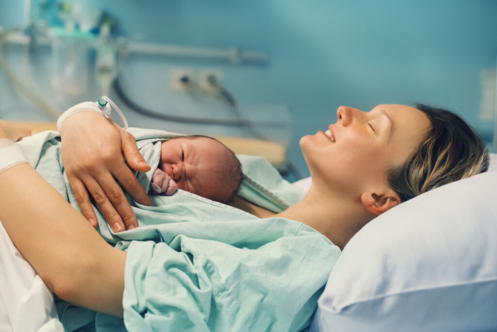 Mulher deitada em cama de hospital com bebê recém-nascido no peito