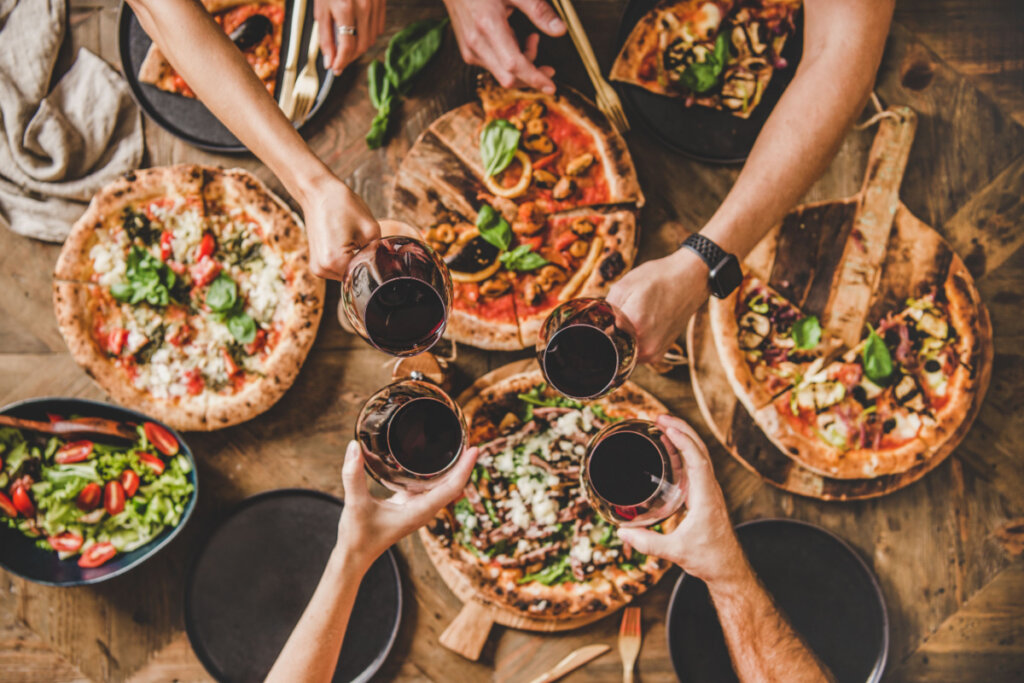 Família ou amigos comendo pizza com vinho.