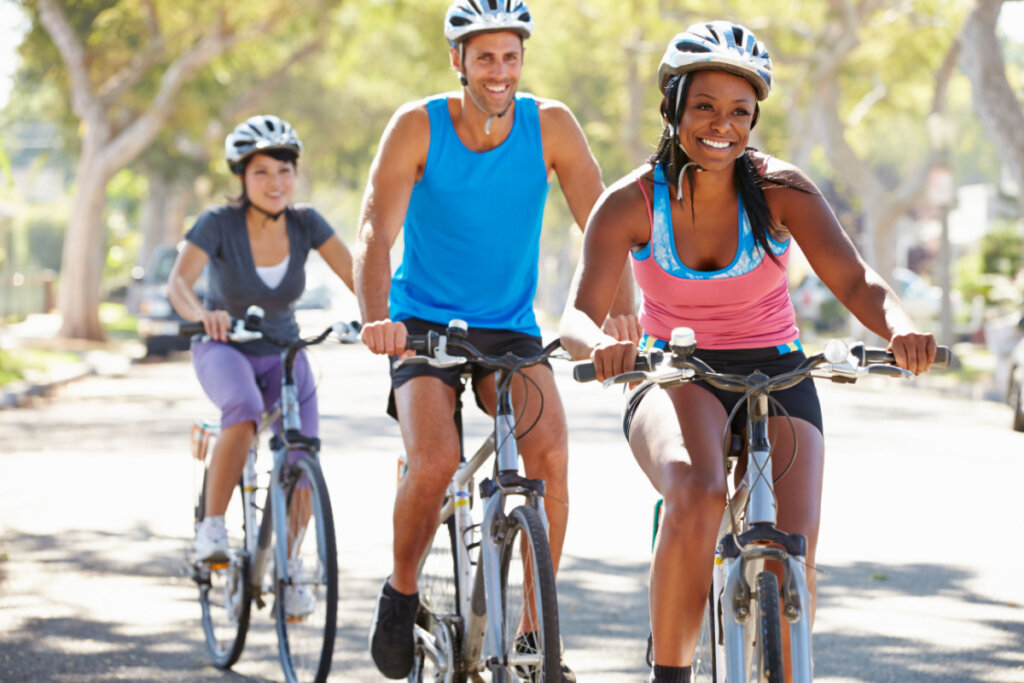 Três pessoas sorridentes andando de bicicleta com capacete.