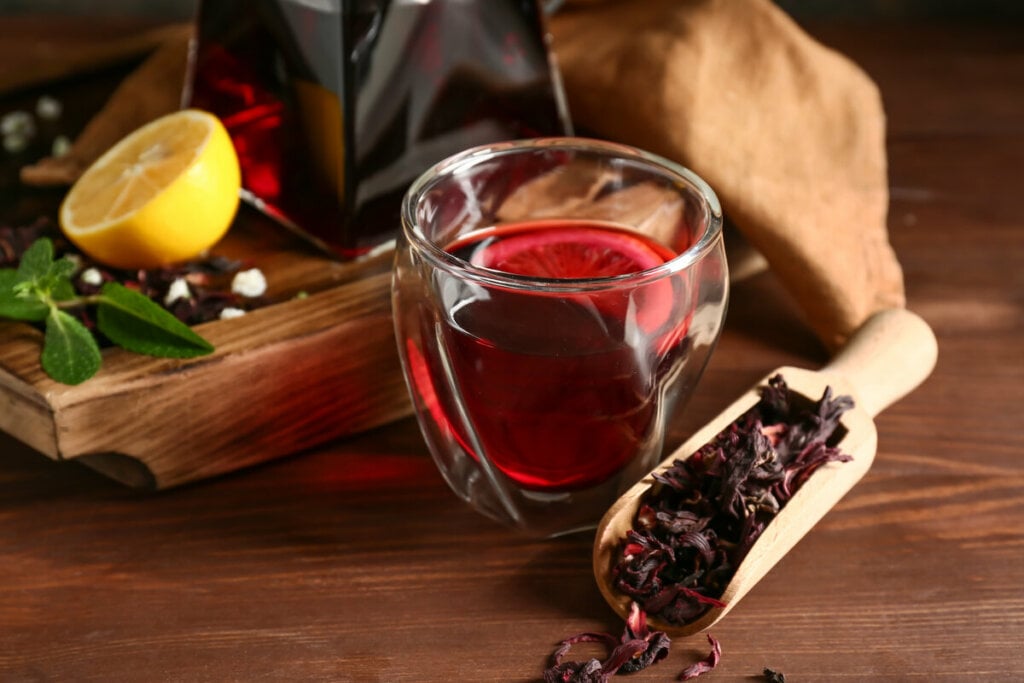 Copo de vidro com chá de hibisco em cima de uma mesa de madeira