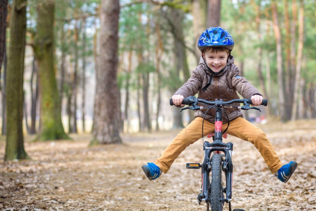 Criança andando de bicicleta com capacete em floresta.