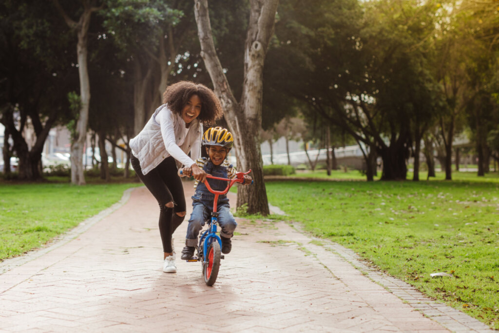 Criança andando de bicicleta junto com a mãe em parque