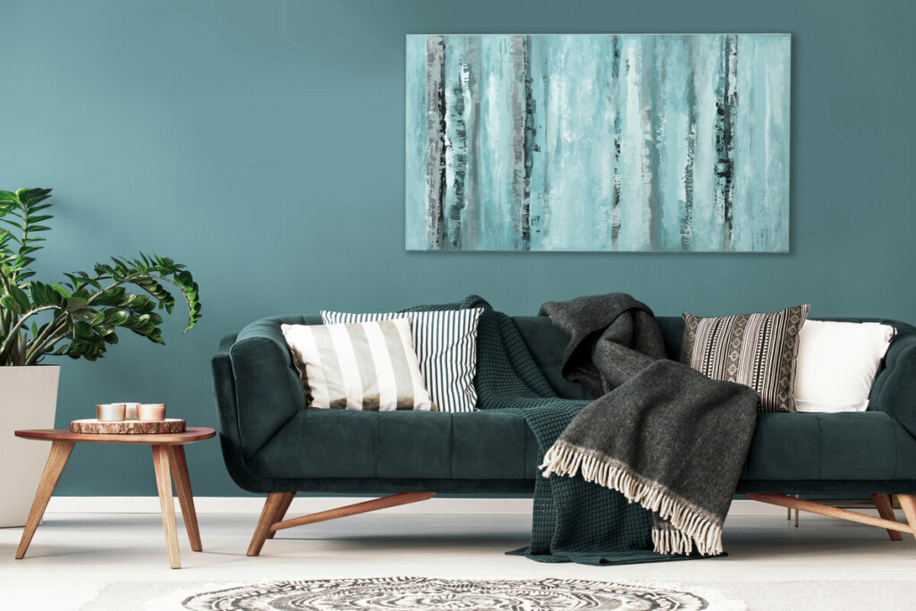 Sala de estar com parede e sofá verde, almofadas, vaso de planta, mesa de madeira e cobertor