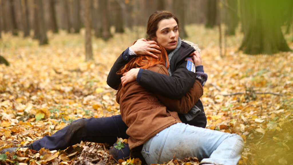 Imagem do filme "A Informante". Policial abraçada com menina em momento de desespero no chão de uma floresta.