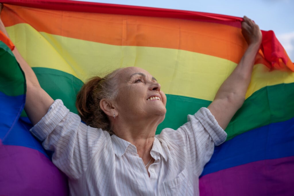 Mulher segurando a bandeira LGBTQIA+ de braços abertos