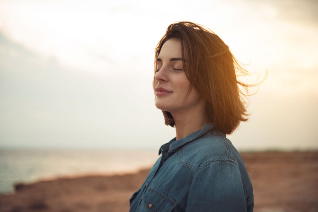 Jovem calma de pé perto do mar com os olhos fechados e expressando relaxamento