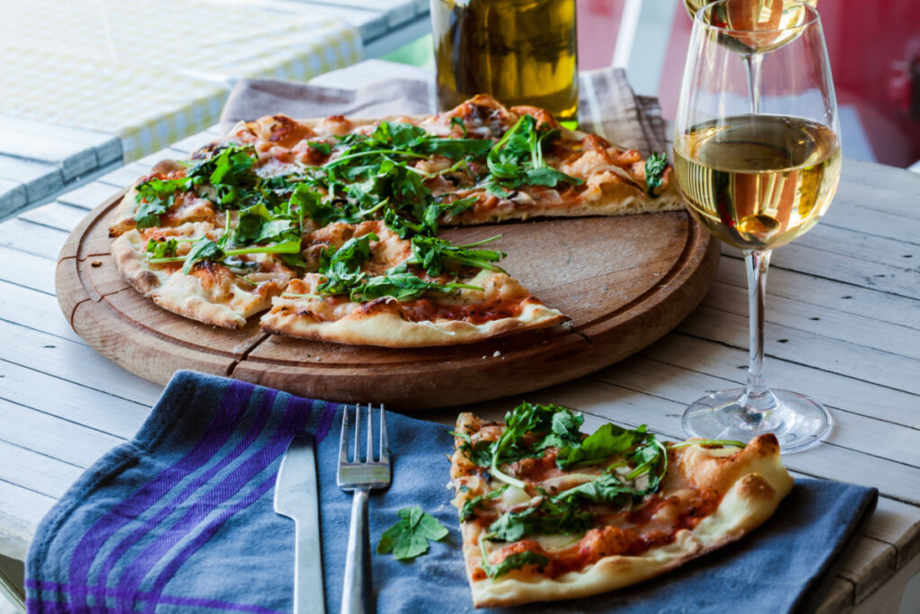 Pizza em tábua de madeira harmonizada com vinho branco.