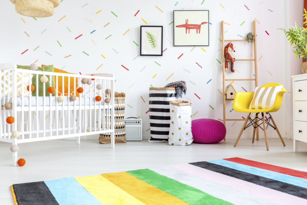Quarto de bebê com cadeira amarela, berço branco, tapete e decorações muito coloridas.