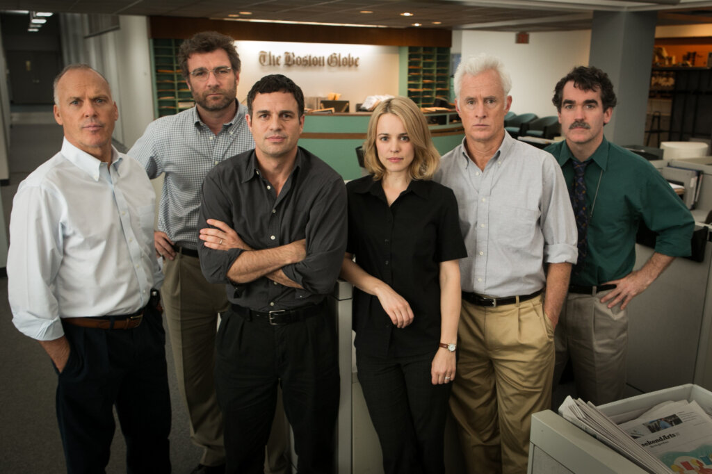 Imagem do filme "Spotlight - Segredos Revelados" com seis jornalistas olhando diretamente para câmera em cenário de redação jornalística.