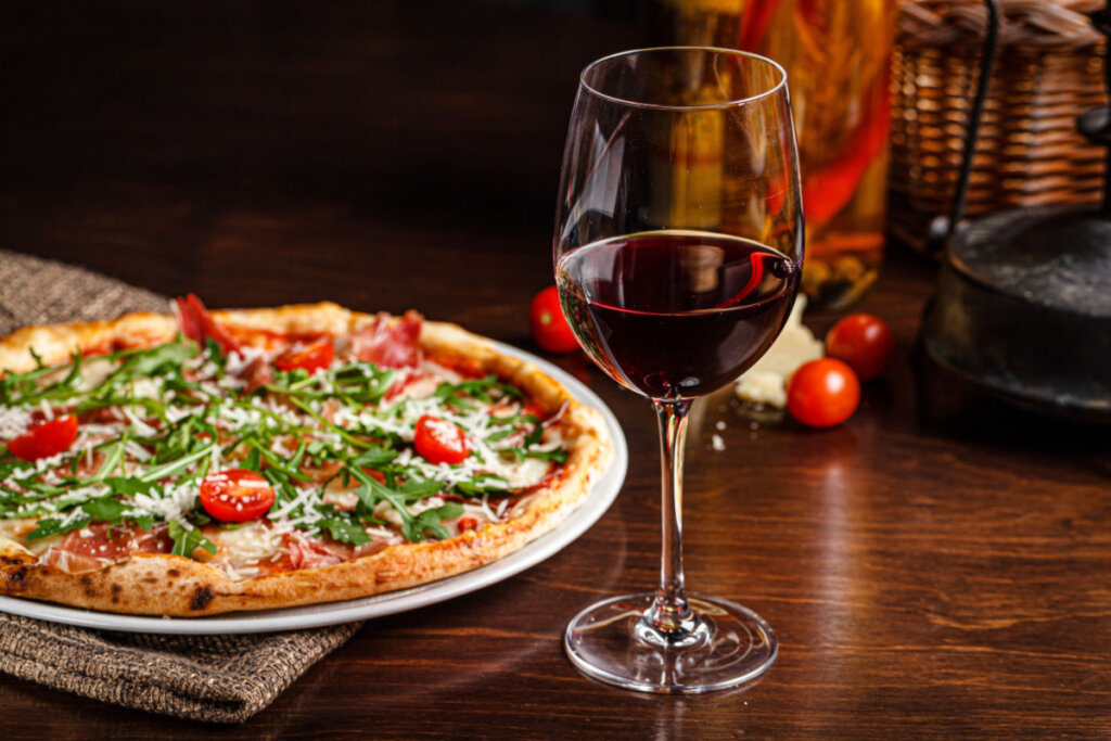 Pizza clássica fina com bordas largas, presunto, tomates-cereja, rúcula, queijo parmesão e vinho tinto.