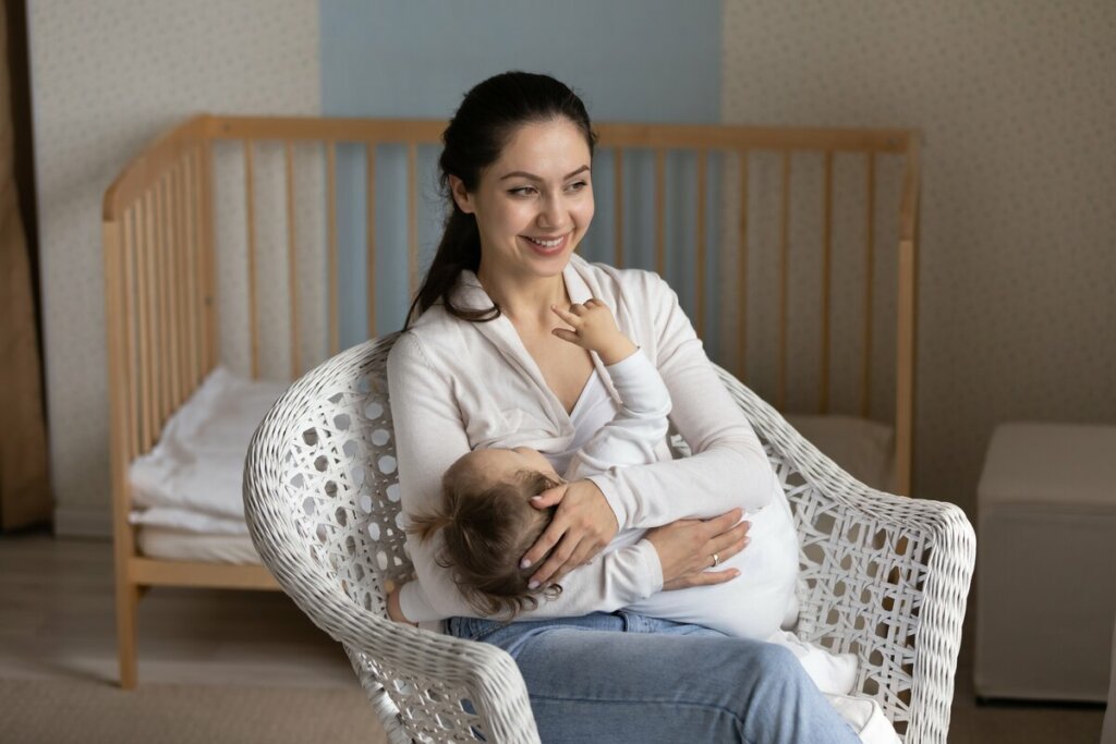 Mulher sentada sorrindo amamentando um bebê