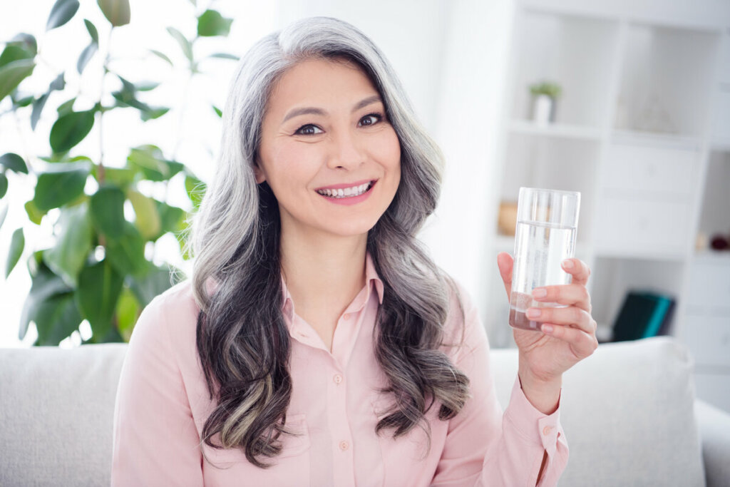 Mulher de meia-idade sorrindo e segurando um copo com água 