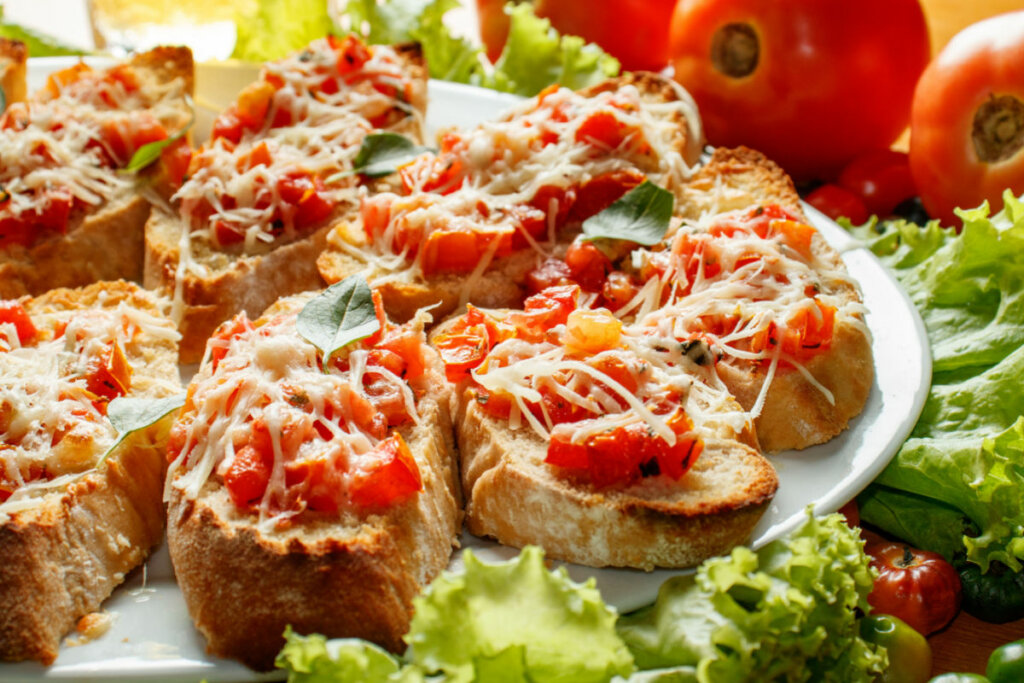 Bruschettas com tomate e queijo em prato branco com folhas de alface embaixo