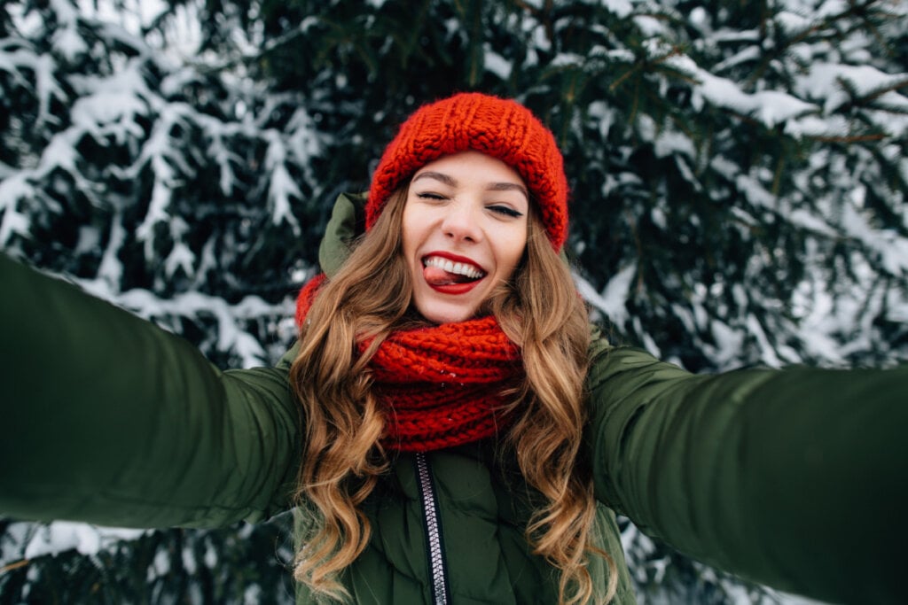 Jovem feliz com touca de malha vermelho e cachecol tirando selfie