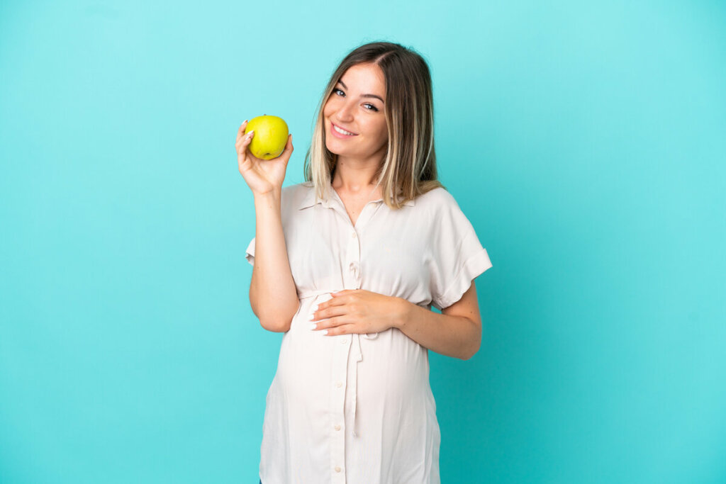 Mulher grávida com vestido branco segurando uma maçã