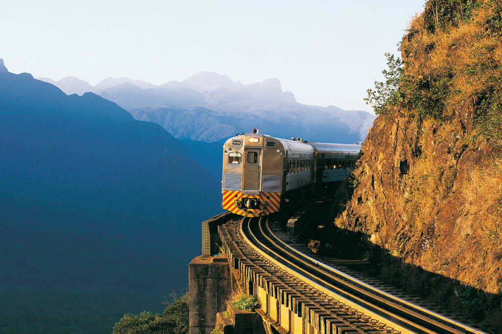 Imagem de trem em trilho com montanhas ao fundo