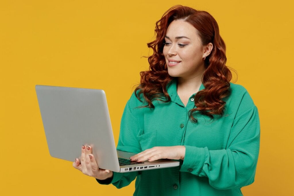 Mulher ruiva com blusa verde mexendo em um notebook