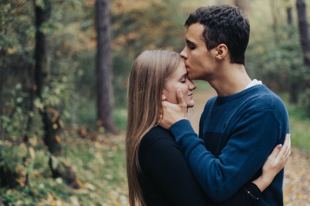 Namorado beijando a testa de namorada em parque.