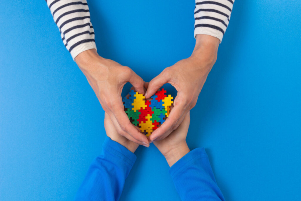 Mãos de adultos e crianças segurando um coração de quebra-cabeça sobre fundo azul claro