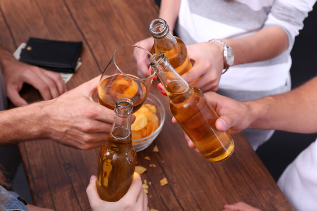 Pessoa brindando com copos e garrafas de cerveja