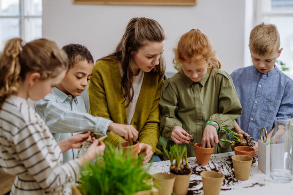 Professora ensinando crianças a cuidarem de pequenas plantas.