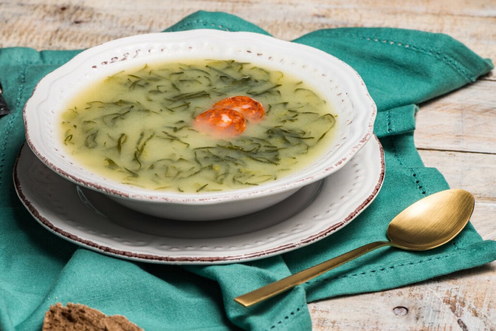 Prato branco com caldo verde em cima de uma mesa de madeira